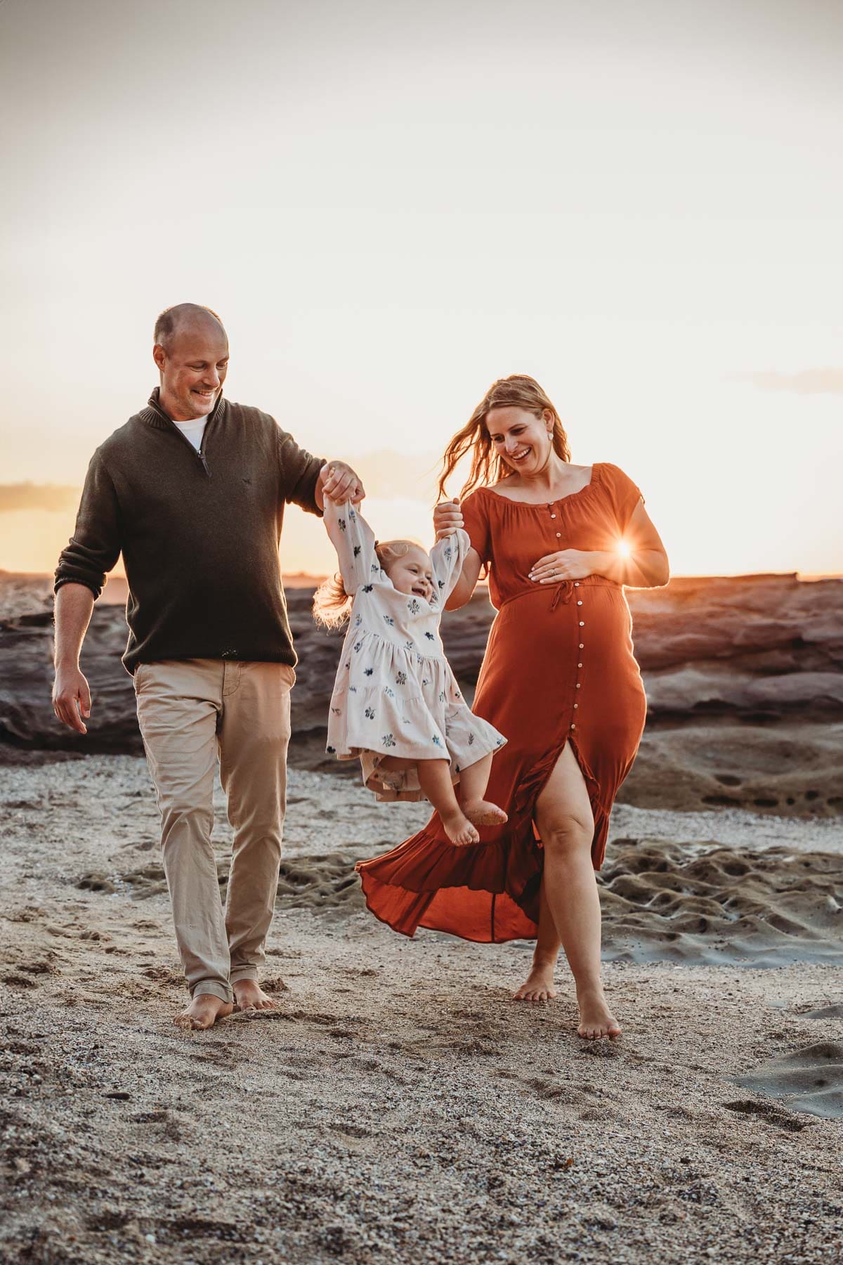 A family walk along the beach at sunset with their baby girl between them