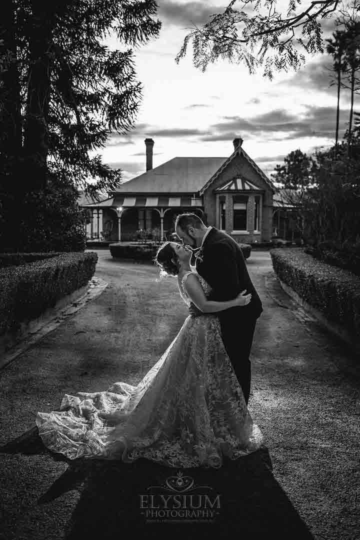 Black and white photograph of a bride and groom standing in the driveway of Burnham Grove at dusk