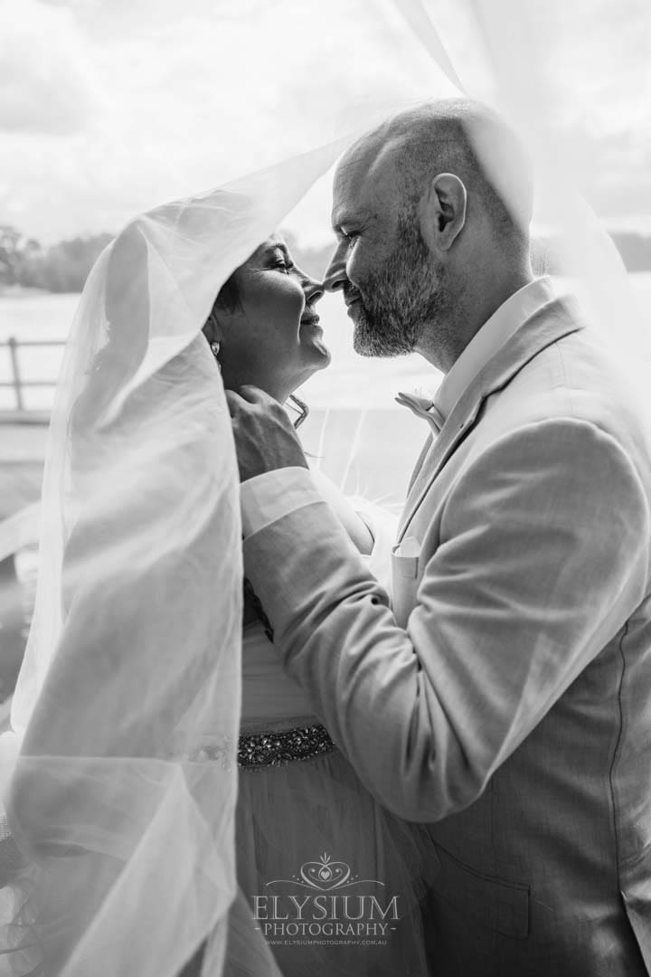 A bride and groom share an almost kiss under the bridal veil