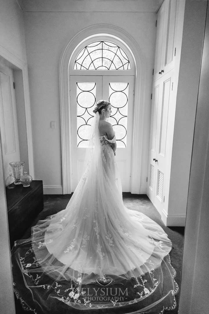 A bride stands beside an arched doorway with her wedding gown flowing across the floor