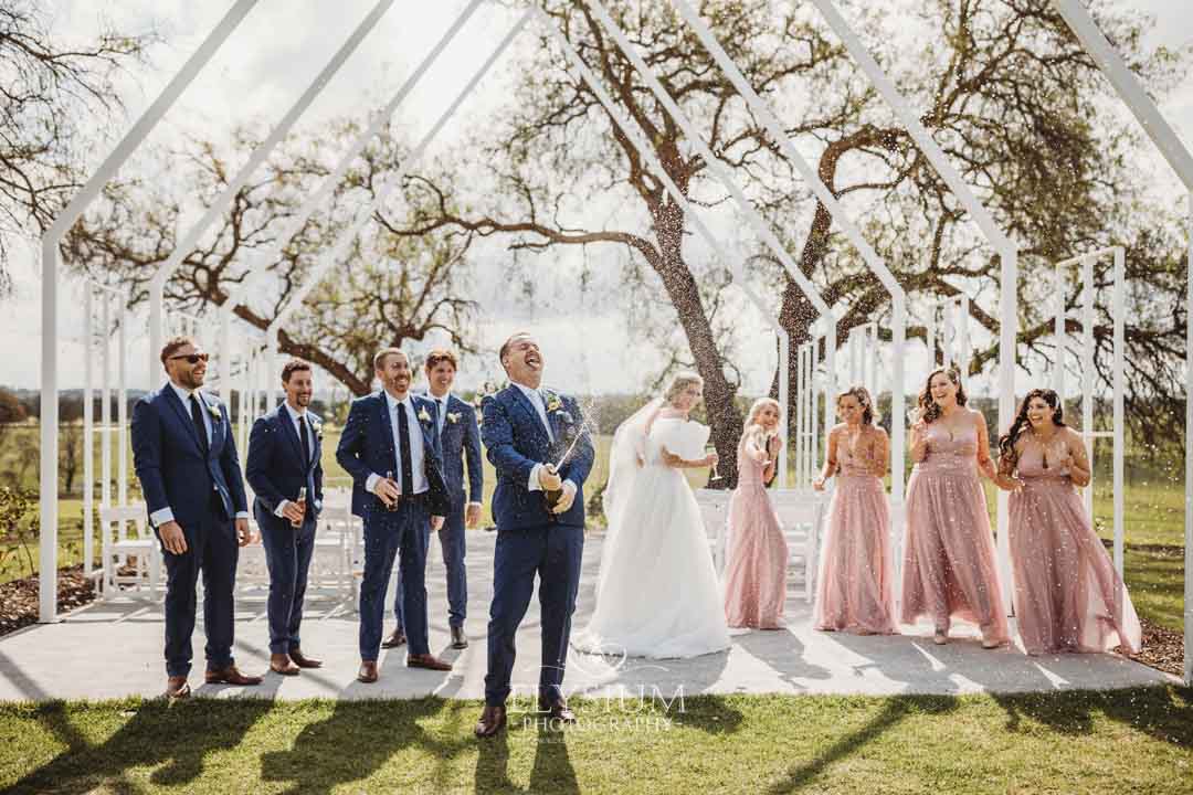 A bridal party spray champagne and laugh after the wedding ceremony