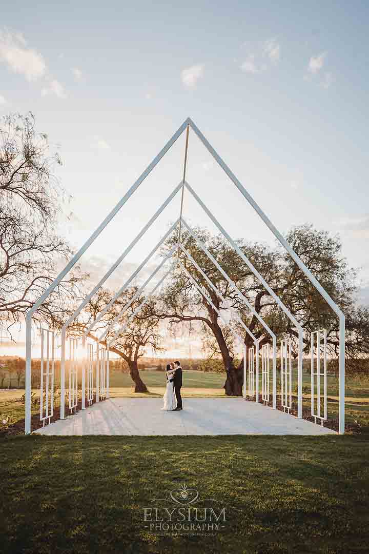 A bride and groom dance in a frame chapel as the sun sets behind them at Burnham Grove