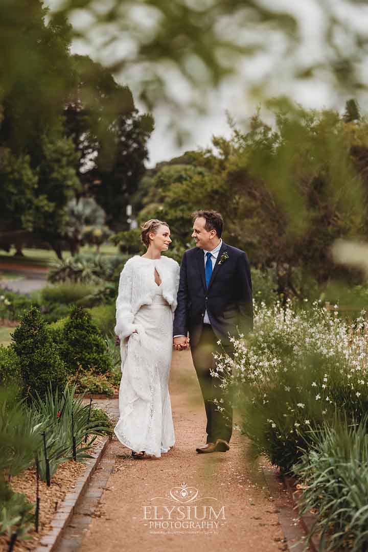 Newlyweds walk along a path through lush gardens after their sydney ceremony