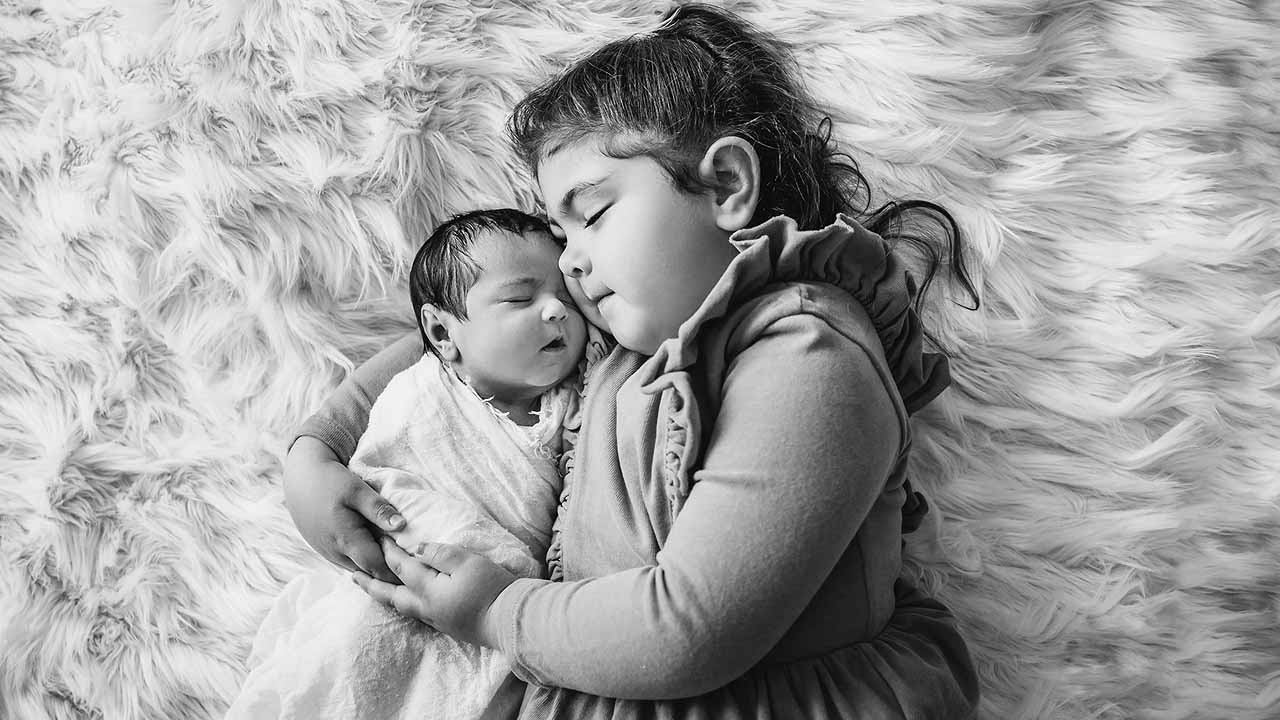 A mother holds her newborn baby in her hands as she lays wrapped on a white blanket