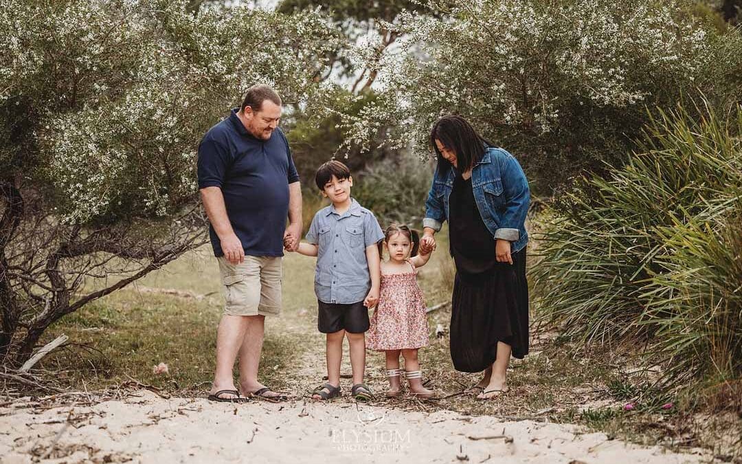 A family hold hands with their children as they stand on a beach surrounded by trees